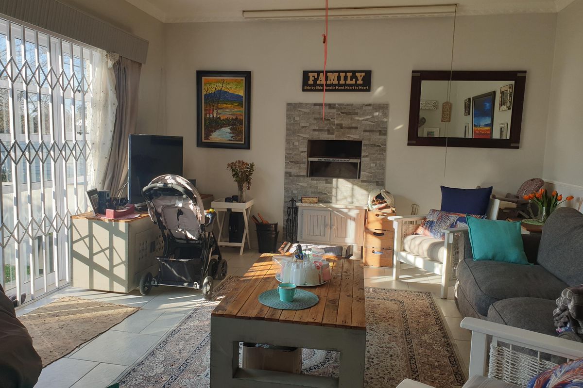 A comfortable living room featuring a built-in fireplace with stone cladding, tiled flooring, and large sliding doors with security gates.