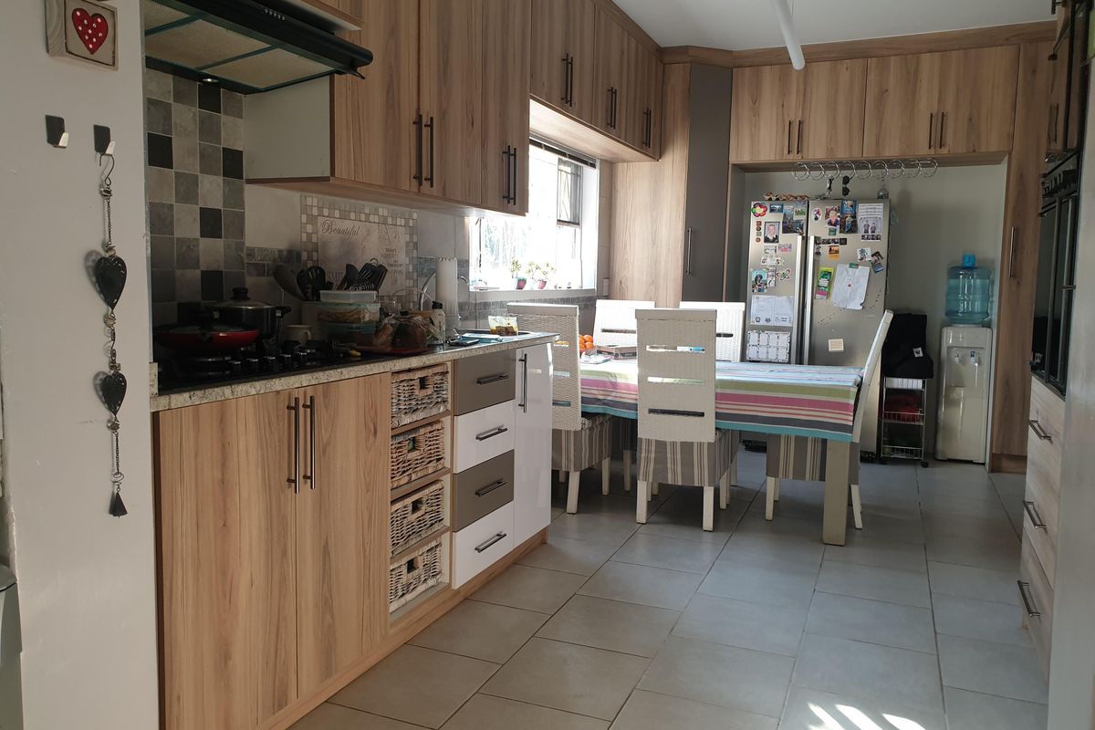 A functional kitchen featuring wood-look cabinetry, a gas hob with extractor fan, tiled backsplash, and integrated oven, with an adjacent dining area.