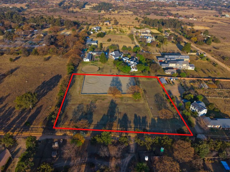 Aerial view of a vacant residential plot featuring a fenced perimeter and an established equestrian arena, situated in a semi-rural residential area.