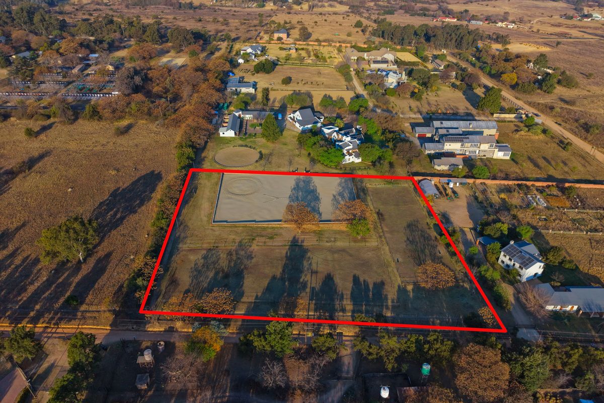 Aerial view of a vacant residential plot featuring a fenced perimeter and an established equestrian arena, situated in a semi-rural residential area.