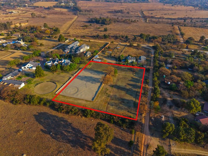 Aerial view of a vacant residential plot featuring a fenced equestrian arena and open land in a rural estate setting.