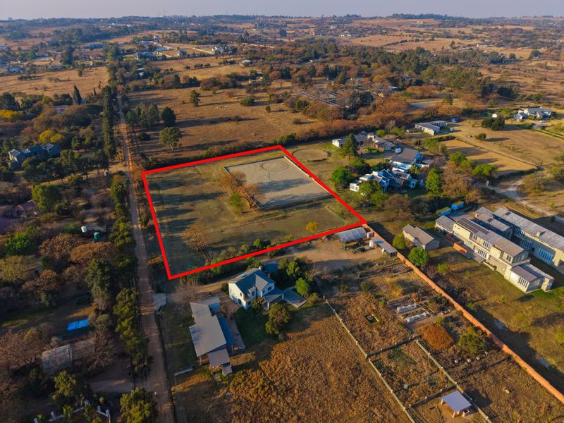 Aerial view of a vacant residential plot with a clearly marked boundary, situated in a semi-rural neighborhood setting.