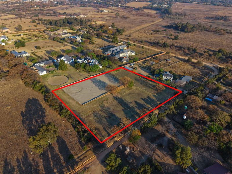 Aerial view of a vacant residential plot featuring a fenced perimeter and an established equestrian arena in a rural setting.