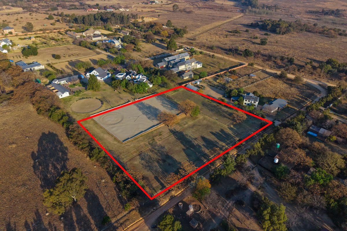 Aerial view of a vacant residential plot featuring a fenced perimeter and an established equestrian arena in a rural setting.