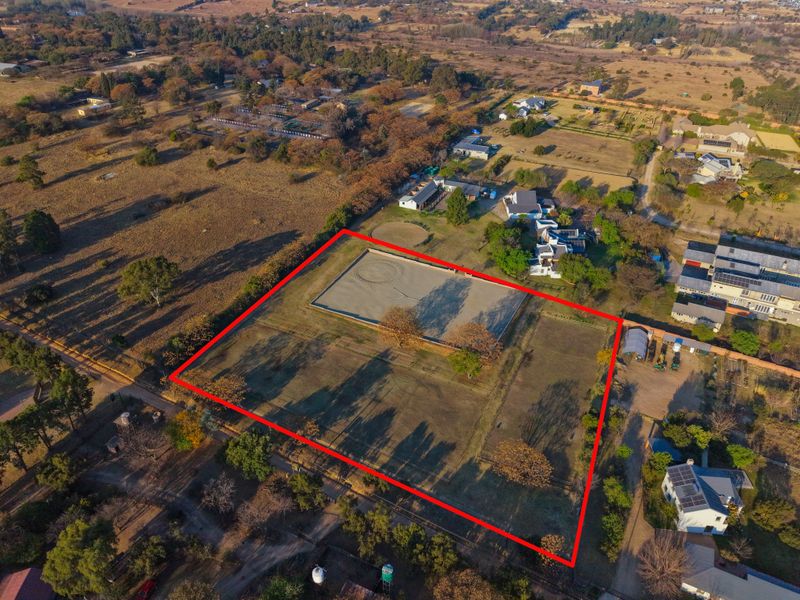 Aerial view of a large, fenced residential vacant land plot featuring an established equestrian arena in a semi-rural setting.