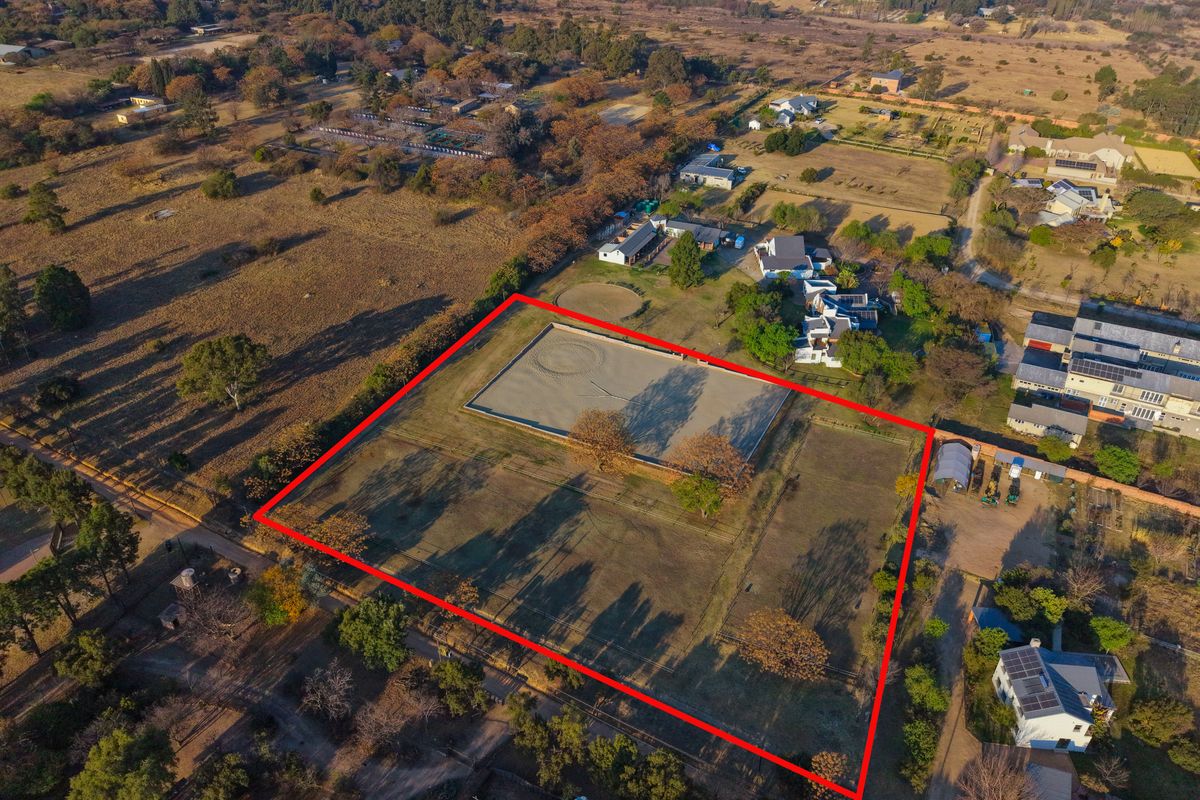 Aerial view of a large, fenced residential vacant land plot featuring an established equestrian arena in a semi-rural setting.