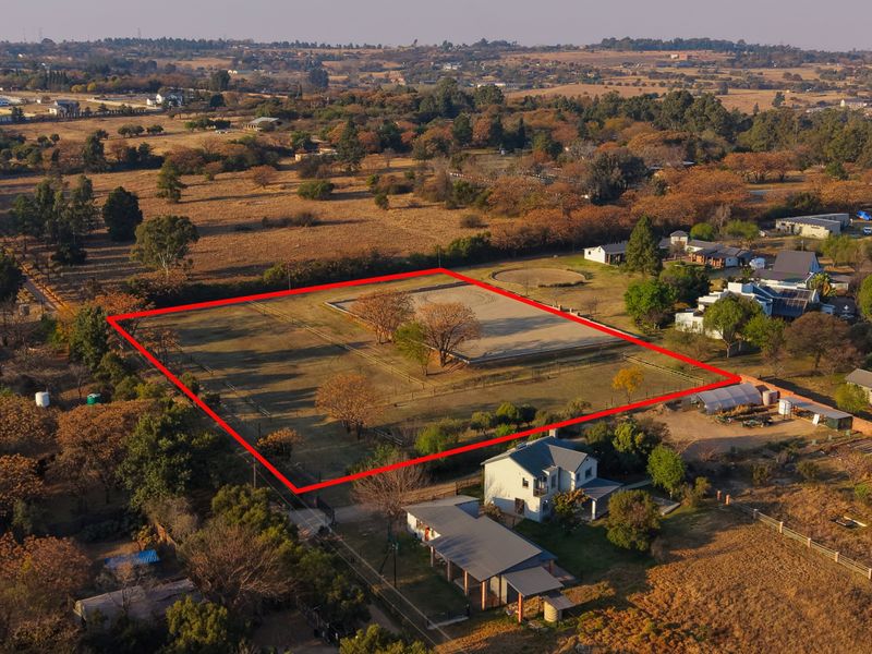 Aerial view of a residential vacant land plot featuring perimeter fencing and an equestrian arena, situated in a semi-rural landscape.