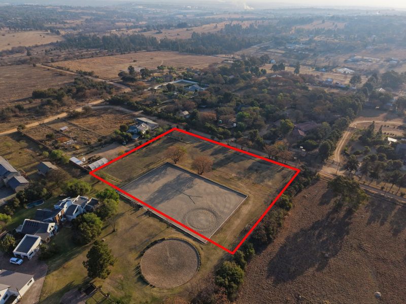 Aerial view of a vacant residential plot featuring an established equestrian arena and round pen, situated in a semi-rural neighborhood.