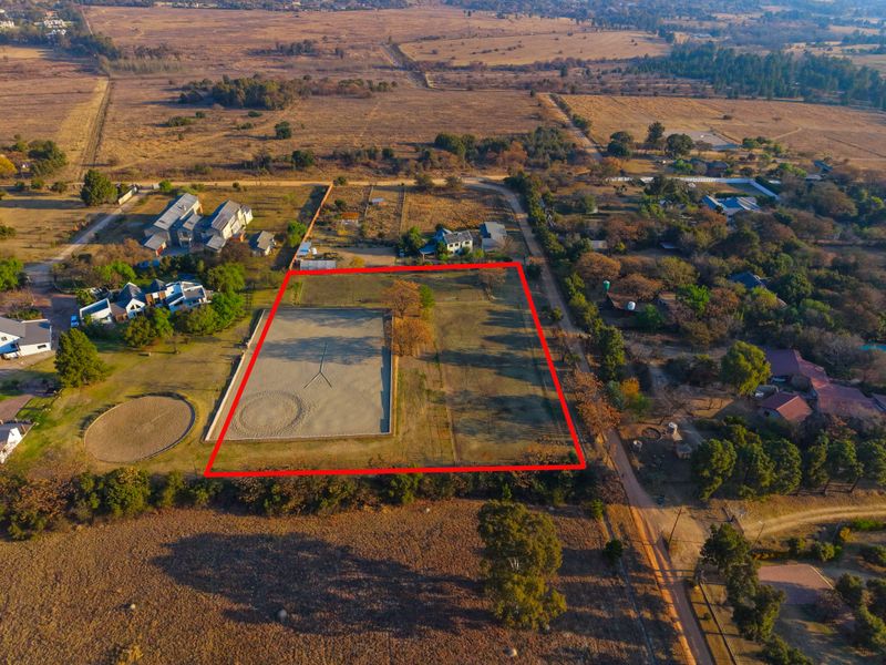 Aerial view of a large, fenced residential vacant land plot featuring an established equestrian arena and open space in a rural setting.