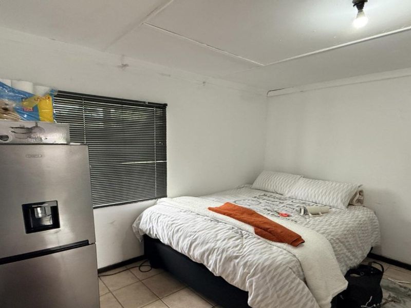 A bedroom featuring tiled flooring and venetian blinds, currently showing signs of wear including ceiling damage and peeling paint.