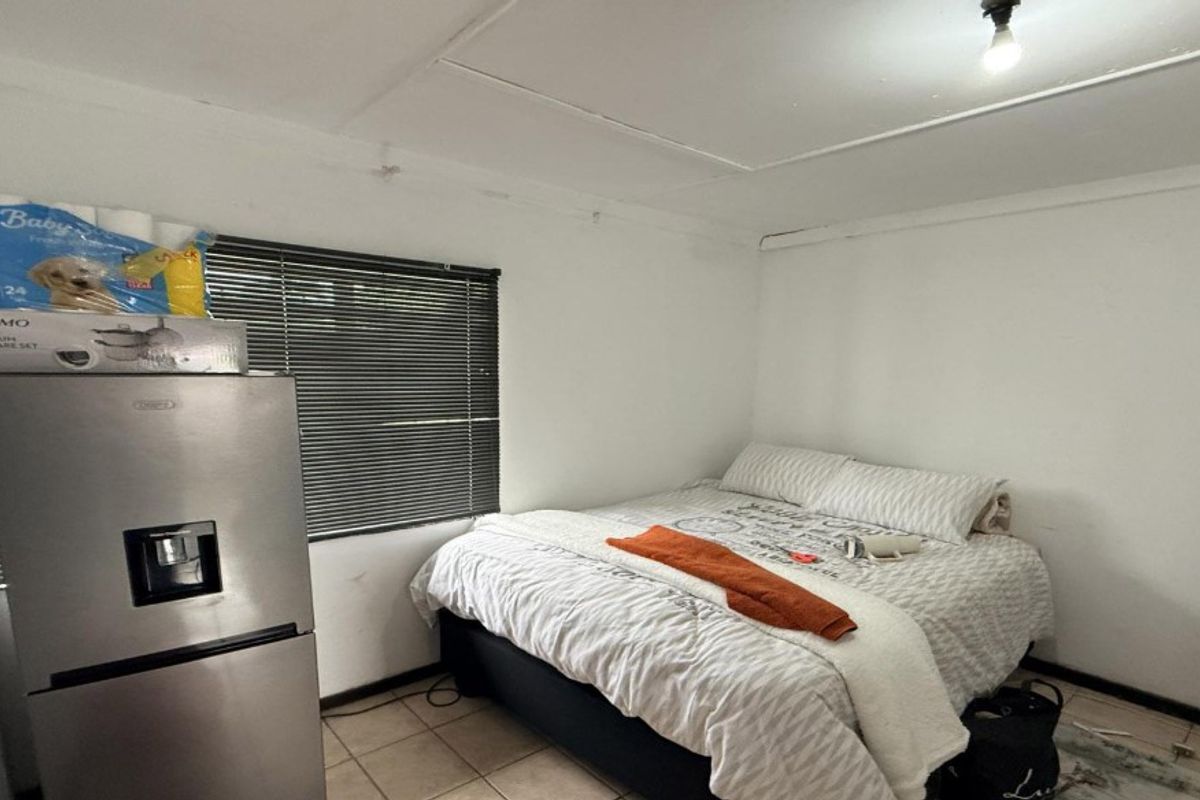 A bedroom featuring tiled flooring and venetian blinds, currently showing signs of wear including ceiling damage and peeling paint.