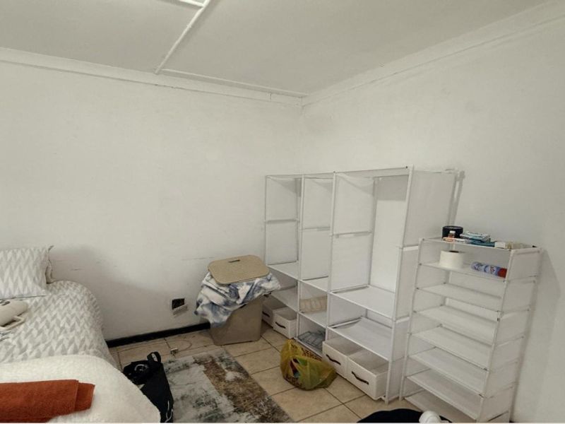 A bedroom featuring tiled flooring and plain white walls, currently used for storage with visible wear on the wall surfaces.