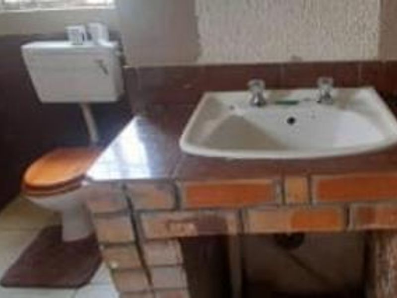 A dated bathroom featuring a brick-based vanity with a ceramic basin and a standard toilet, requiring cosmetic updates to improve functionality and aesthetic appeal.