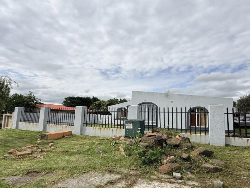 Front exterior view of a single-story house featuring a perimeter wall with metal security fencing and arched window detailing.