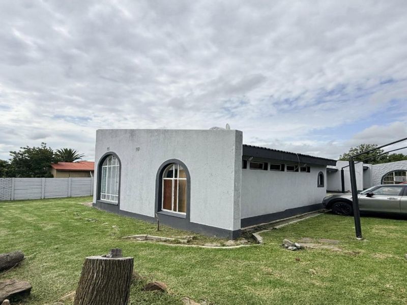 Rear view of the property featuring arched windows, textured plaster finish, and a surrounding precast concrete boundary wall set within a grassed yard.