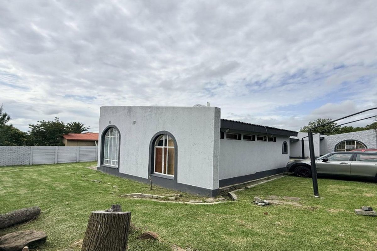 Rear view of the property featuring arched windows, textured plaster finish, and a surrounding precast concrete boundary wall set within a grassed yard.