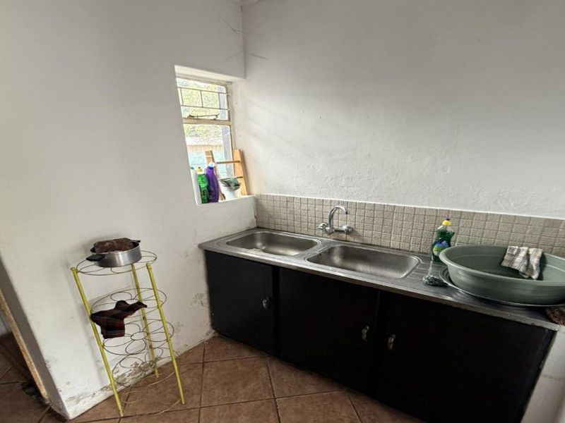 A functional laundry area featuring a double stainless steel sink, tiled splashback, and built-in cabinetry, requiring some cosmetic updates to the walls and finishes.