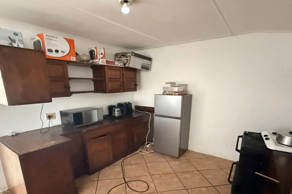 A functional kitchen space featuring wooden cabinetry, tiled flooring, and ample counter space, offering potential for modernization and aesthetic updates.