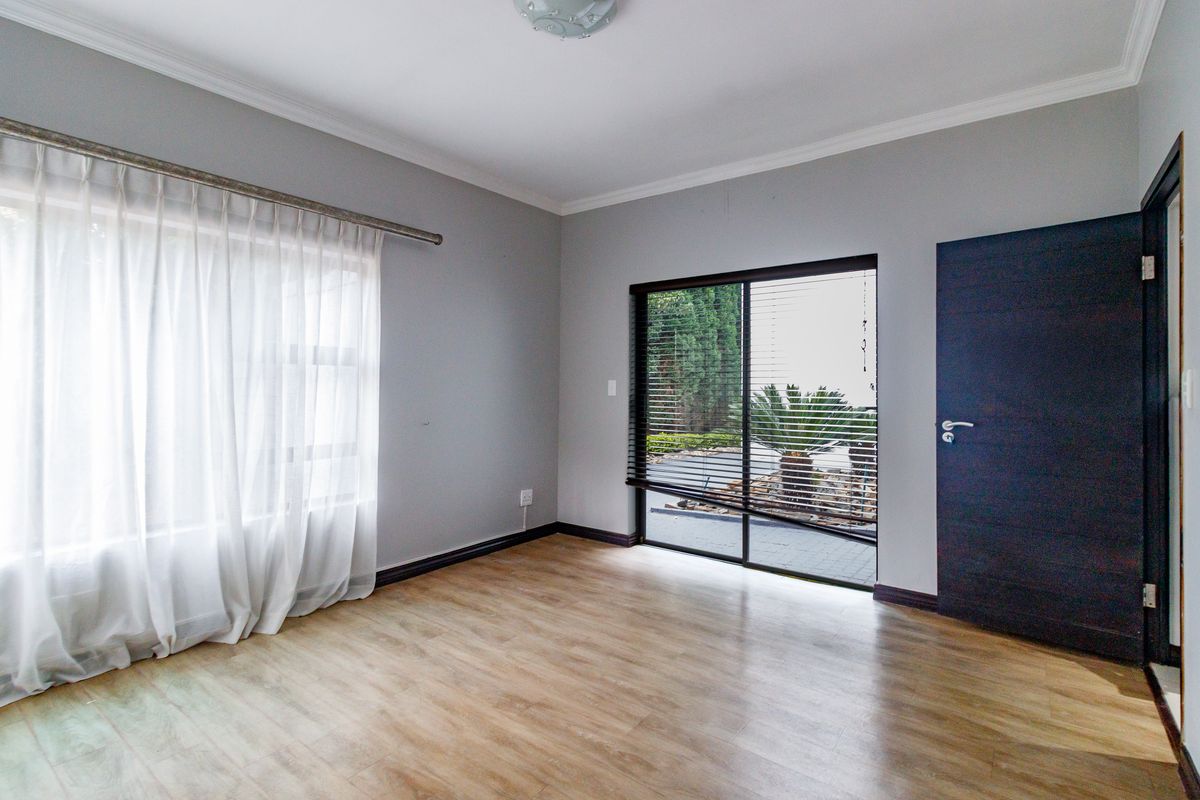 A bright, empty bedroom featuring light wood-look laminate flooring, neutral grey walls, and a sliding glass door providing access to the garden.