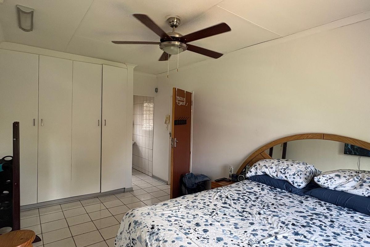 A bedroom featuring built-in wardrobes, tiled flooring, and a ceiling fan, with an adjoining en-suite bathroom visible through the doorway.