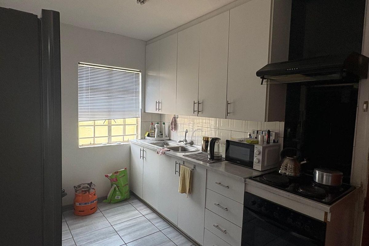 A functional kitchen featuring white cabinetry, tiled splashbacks, a built-in oven with extractor fan, and tiled flooring.