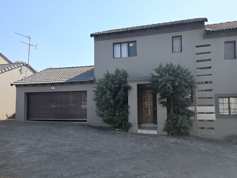 Front elevation of a double-storey townhouse featuring a paved driveway, integrated roller shutter garage, and a timber entrance door.