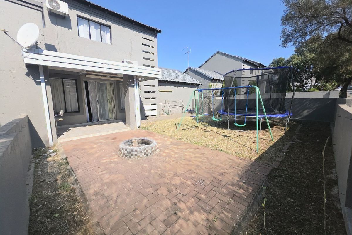 Rear exterior view of the townhouse featuring a paved patio area with a built-in fire pit and a private garden space.
