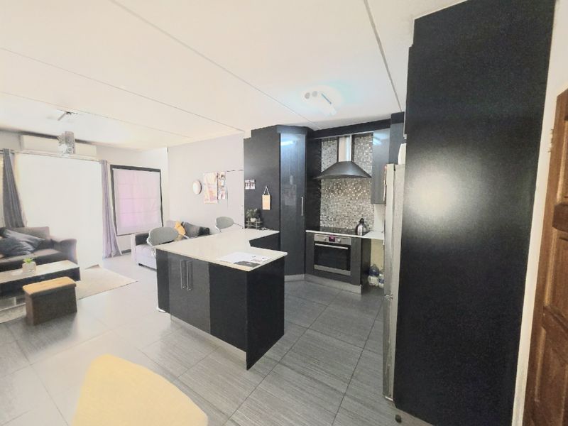 Open-plan living area featuring a modern kitchen with dark cabinetry, a central island, and tiled flooring throughout the combined space.