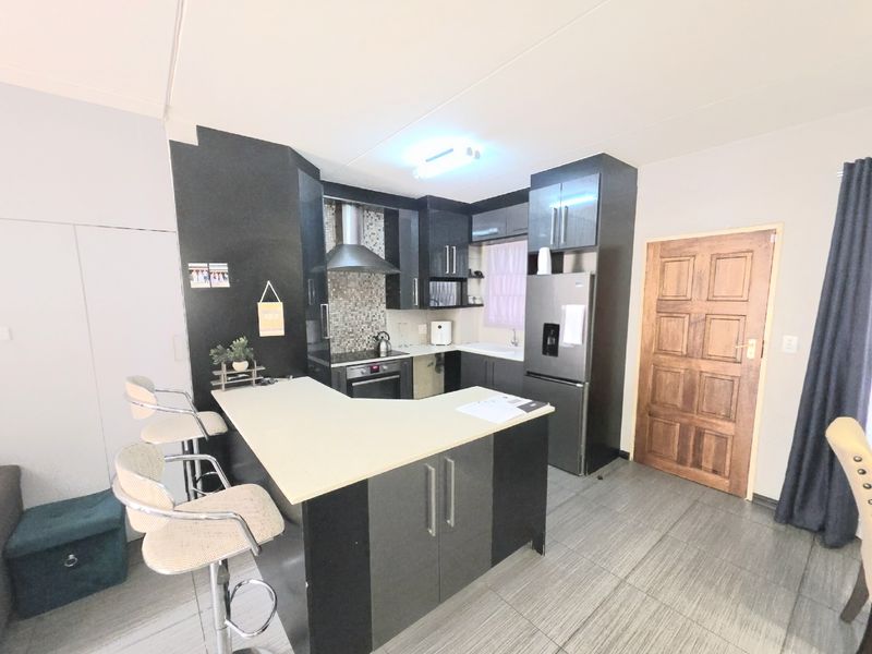 Modern kitchen featuring dark cabinetry, a breakfast nook, built-in oven with extractor fan, and tiled flooring.