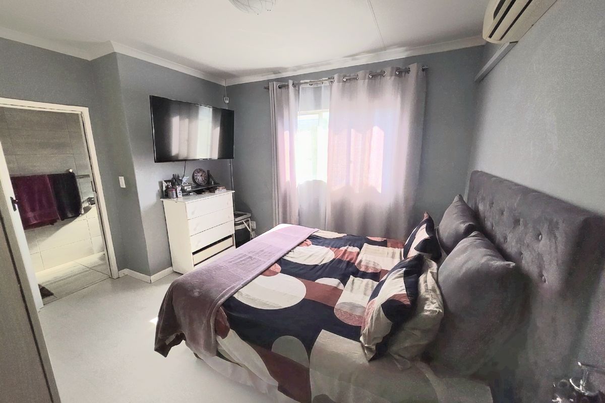 A bedroom featuring an en-suite bathroom, wall-mounted air conditioning unit, and neutral wall finishes.