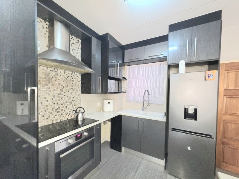 Modern kitchen featuring dark cabinetry, mosaic tile backsplash, stainless steel extractor fan, built-in oven, electric hob, and a functional sink area.