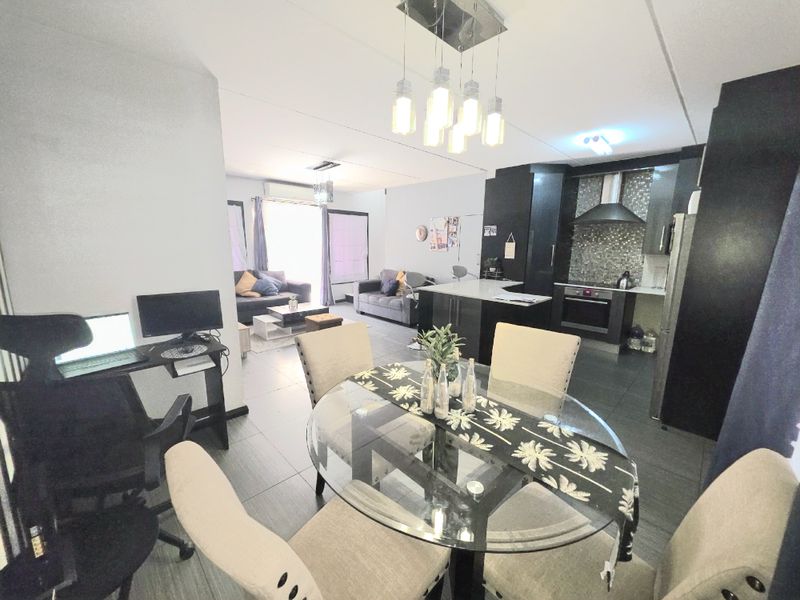 Open-plan living and dining area featuring a modern kitchen with dark cabinetry, a central island, and tiled flooring throughout.