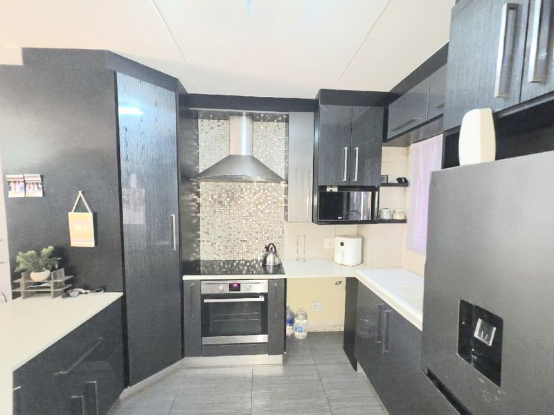 Modern kitchen featuring dark cabinetry, mosaic tile splashback, built-in oven, electric hob, and stainless steel extractor fan.