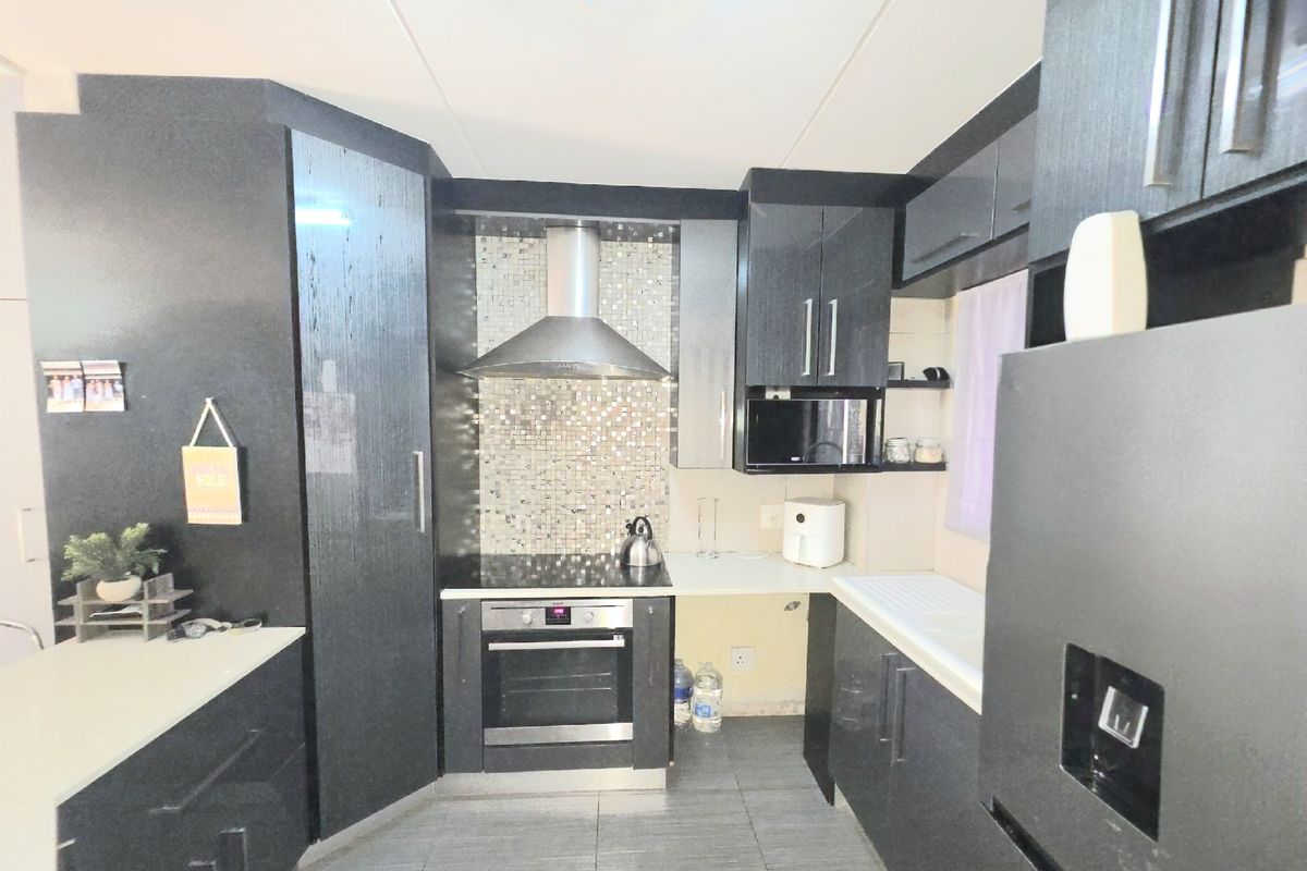 Modern kitchen featuring dark cabinetry, mosaic tile splashback, built-in oven, electric hob, and stainless steel extractor fan.