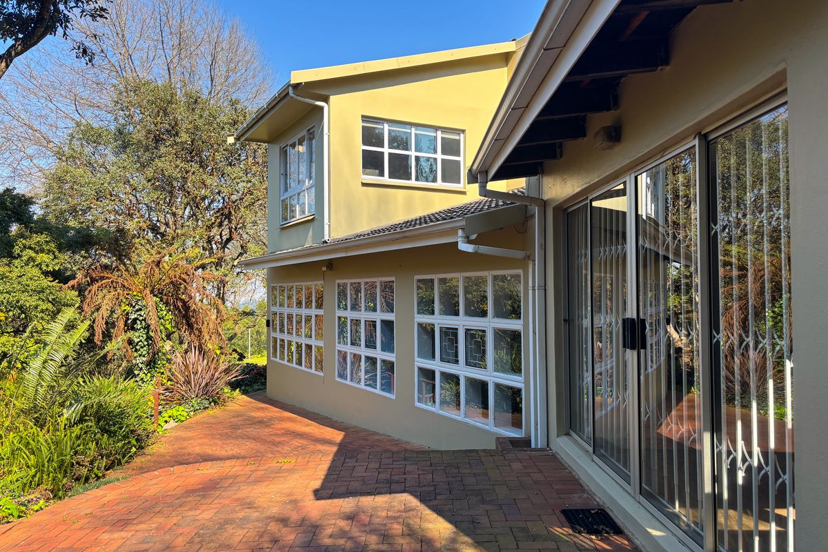 Rear exterior view of the house featuring a brick paved patio, sliding glass doors with security gates, and multi-pane windows.