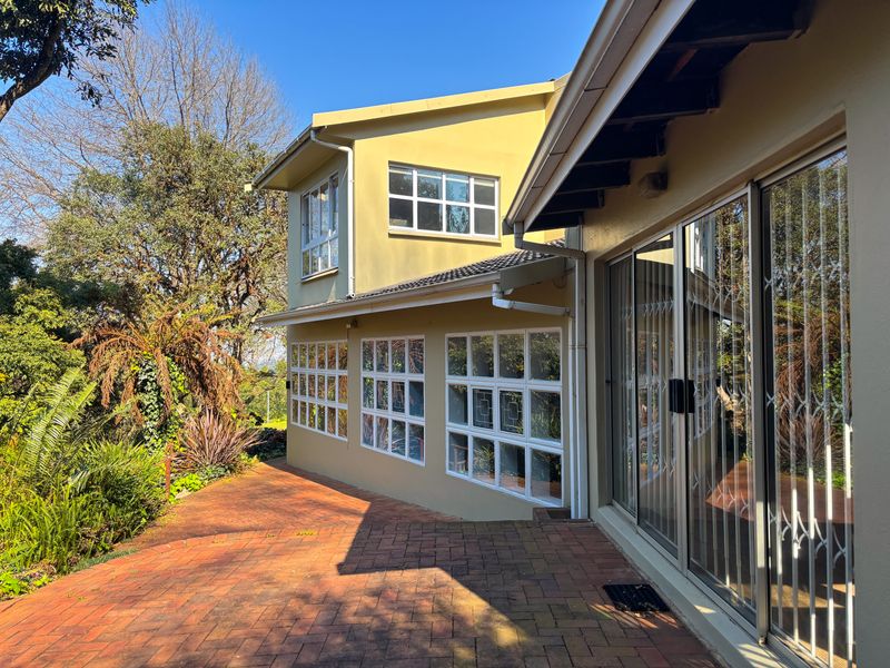 Rear exterior view of the house featuring a brick paved patio, sliding glass doors with security gates, and multi-pane windows.