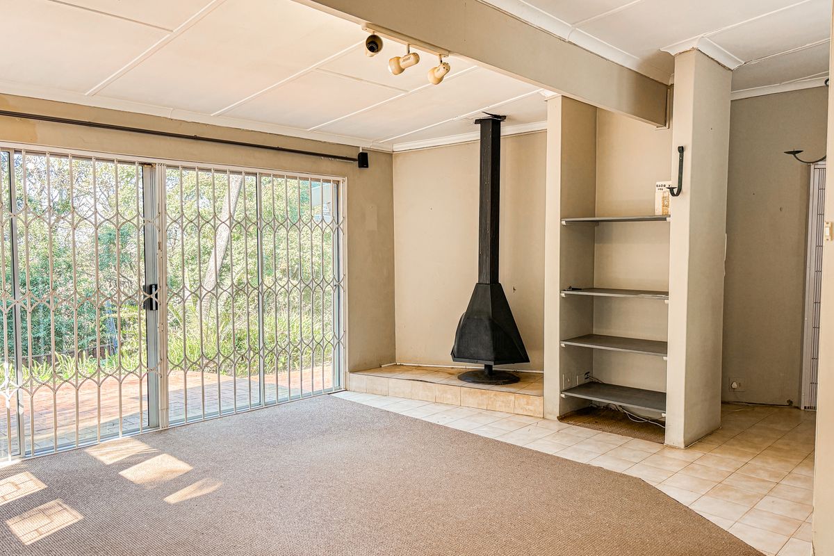 Spacious living area featuring a freestanding fireplace, built-in shelving, and large sliding glass doors with security gates leading to the outdoor patio.