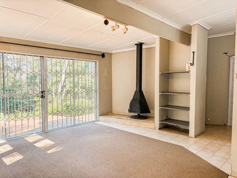 Spacious living area featuring a freestanding fireplace, built-in shelving, and large sliding glass doors with security gates leading to the outdoor patio.