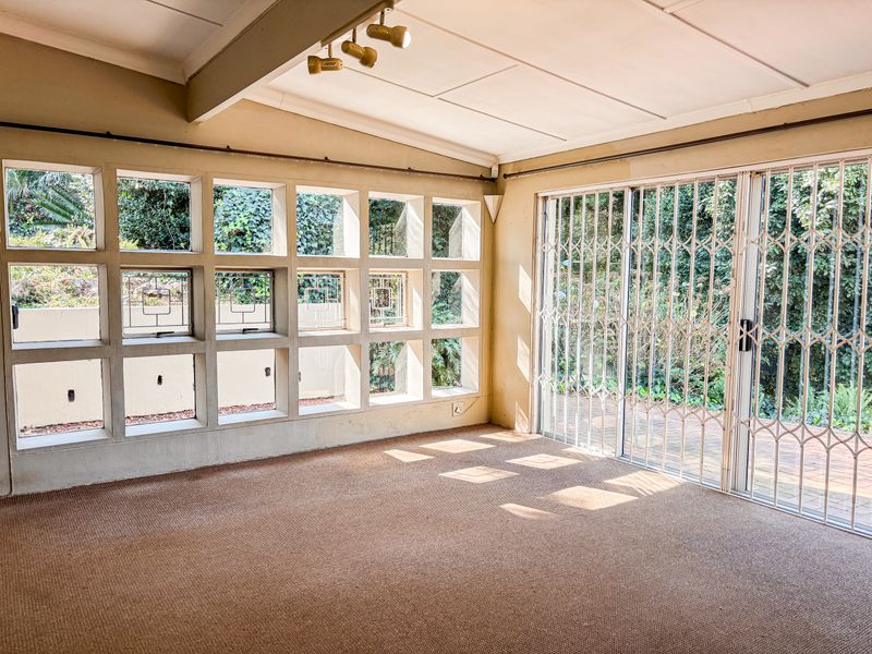 Spacious living area featuring unique grid-pattern windows, track lighting, and sliding glass doors with security gates leading to the outdoor patio.