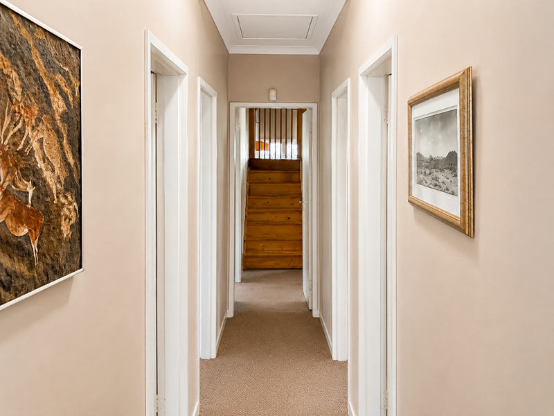 A neutral-toned hallway featuring carpeted flooring, multiple doorways, and a timber staircase leading to an upper level.