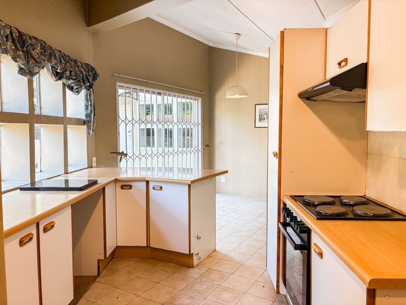 A dated kitchen featuring built-in cabinetry, laminate countertops, and an integrated electric hob and oven, with tiled flooring and direct access to the living area.