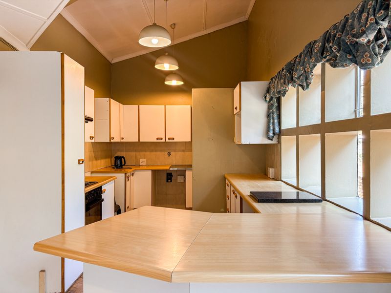 A functional kitchen featuring built-in cabinetry, laminate countertops, and a built-in oven, with a vaulted ceiling and natural light from a large window.