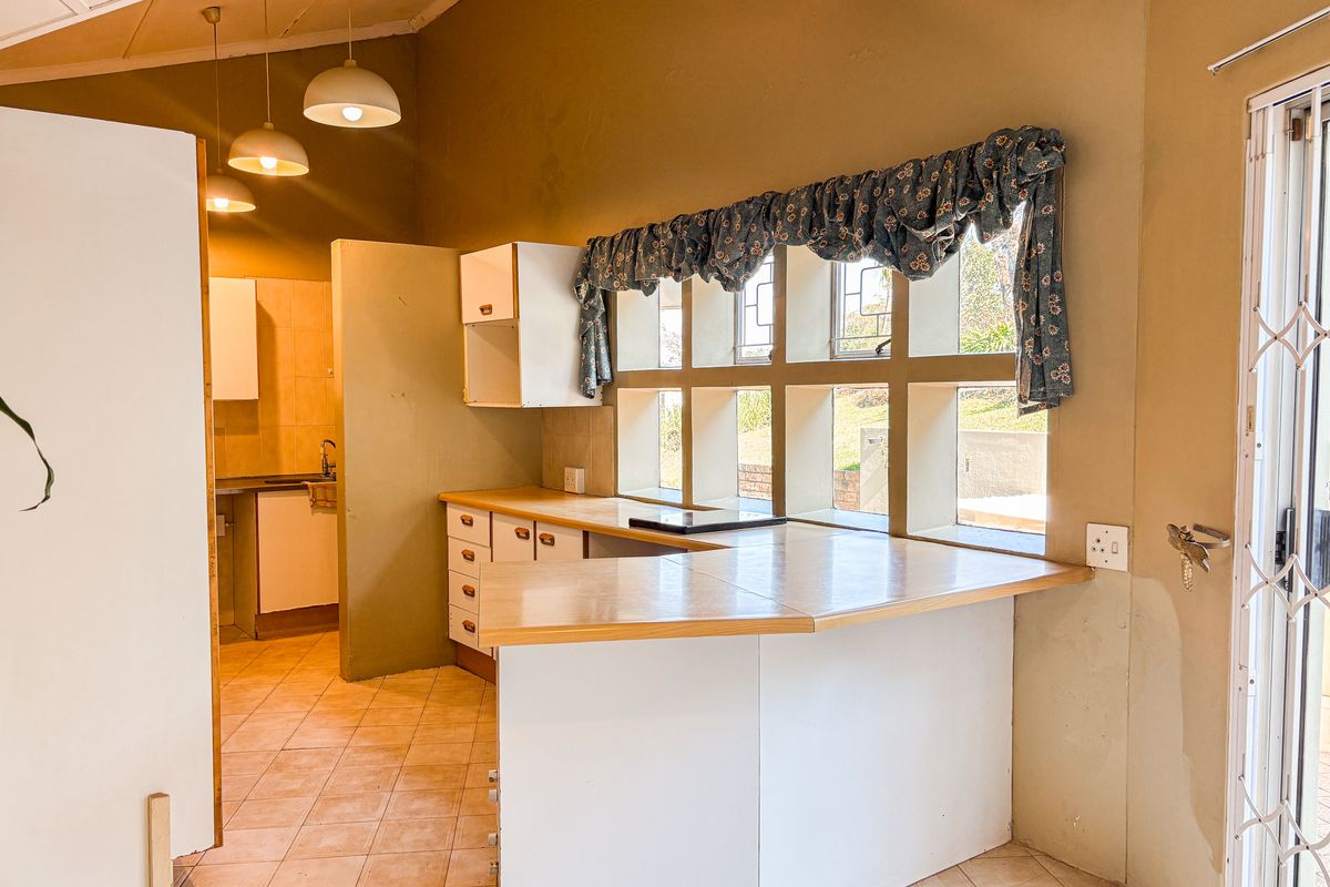 A dated kitchen featuring built-in cabinetry, laminate countertops, and tiled flooring, with a functional layout and natural light from multi-pane windows.