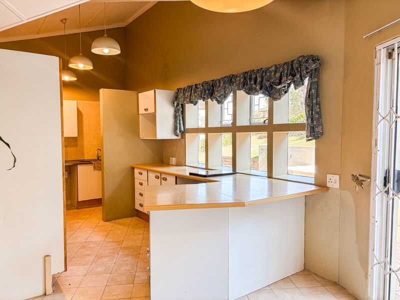 A dated kitchen featuring built-in cabinetry, laminate countertops, and tiled flooring, with a functional layout and natural light from multi-pane windows.
