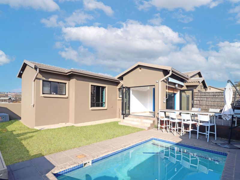 Rear exterior view featuring a swimming pool, timber deck, and bi-fold doors leading into the home, complemented by a landscaped garden area.