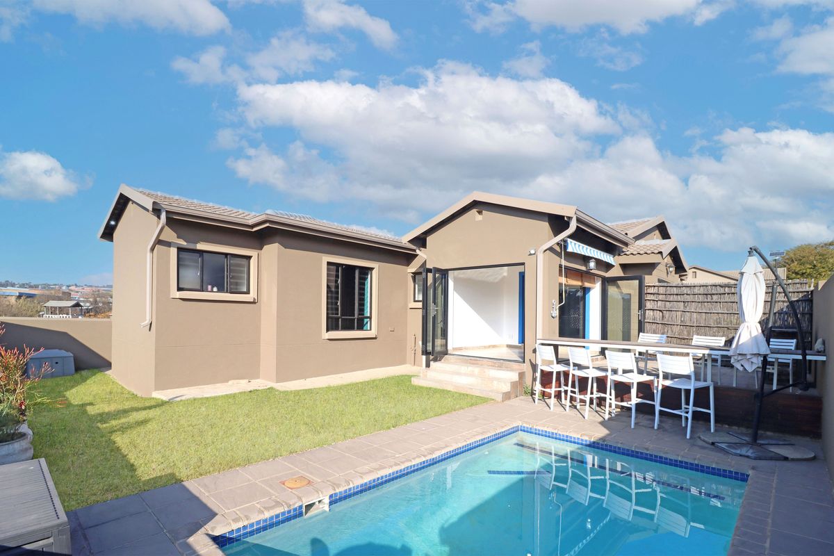 Rear exterior view featuring a swimming pool, timber deck, and bi-fold doors leading into the home, complemented by a landscaped garden area.