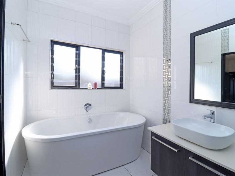 A modern, clean bathroom featuring a white freestanding bathtub, a vessel sink on a dark vanity cabinet, and neutral wall tiling.