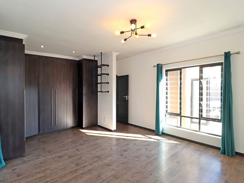 Spacious bedroom featuring dark wood built-in cupboards, laminate flooring, modern lighting, and an air conditioning unit.