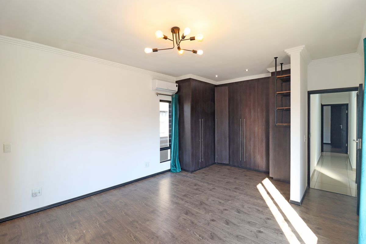 A spacious, well-lit bedroom featuring dark wood-toned built-in cupboards, laminate flooring, and an integrated air conditioning unit.