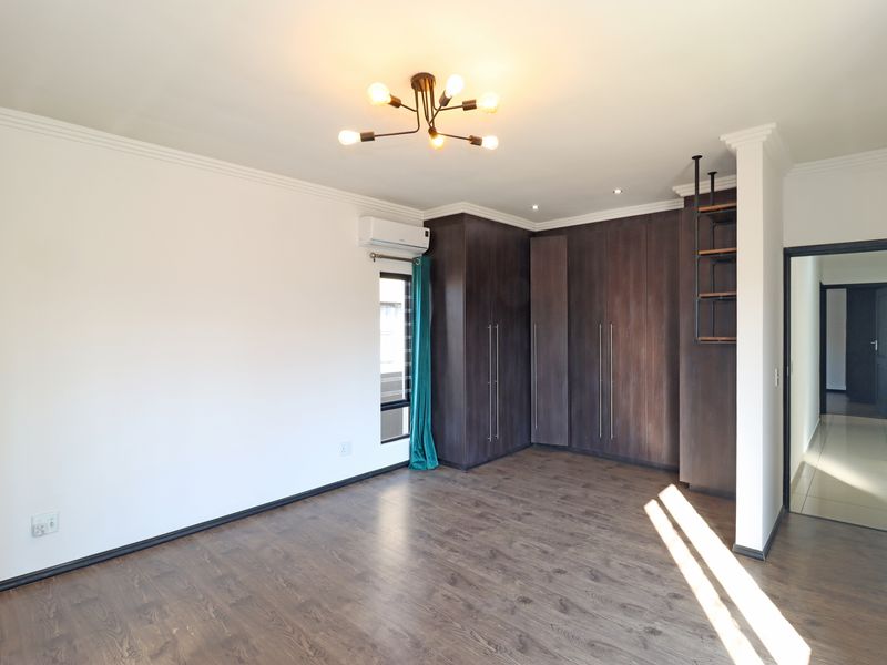 A spacious, well-lit bedroom featuring dark wood-toned built-in cupboards, laminate flooring, and an integrated air conditioning unit.